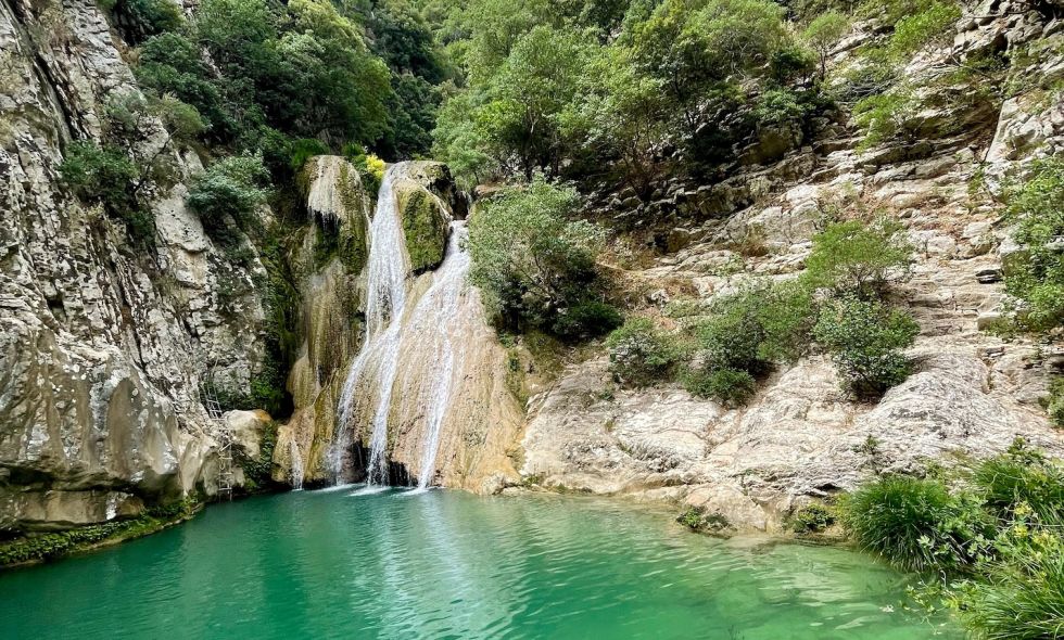 Polylimnio Waterfall pours into green pool under a blue sky in the Kalamata region of Greece